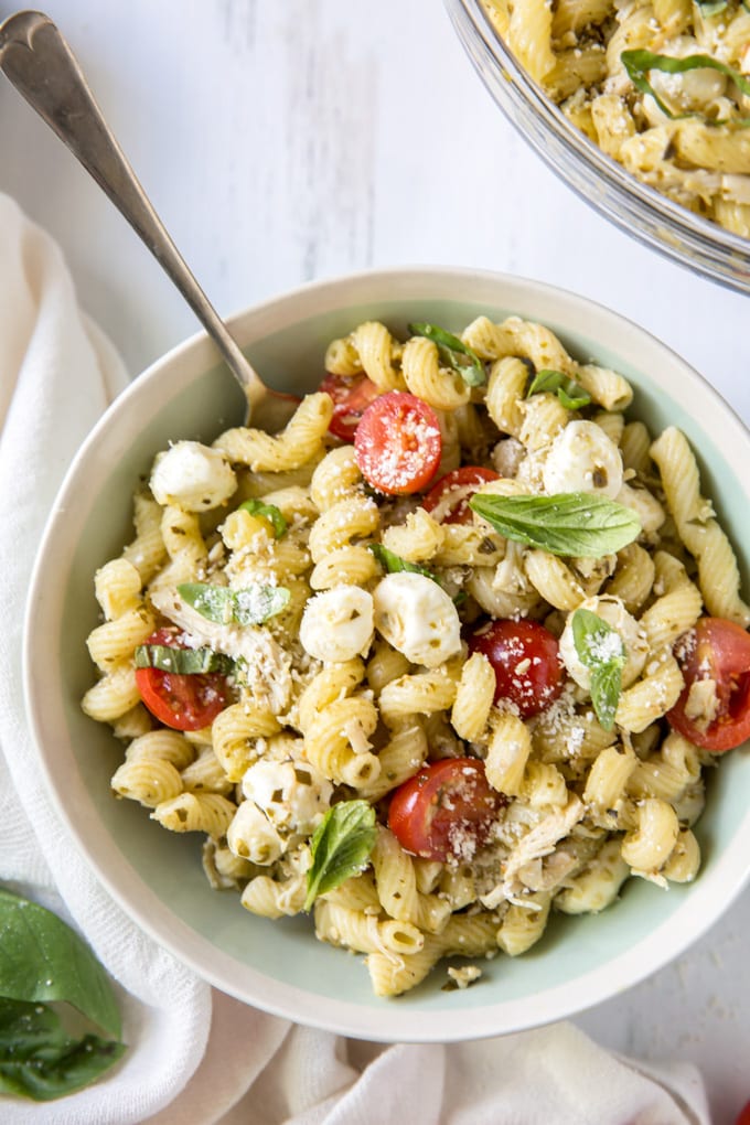 Bowl of chicken pesto pasta salad with tomatoes and mozzarella.