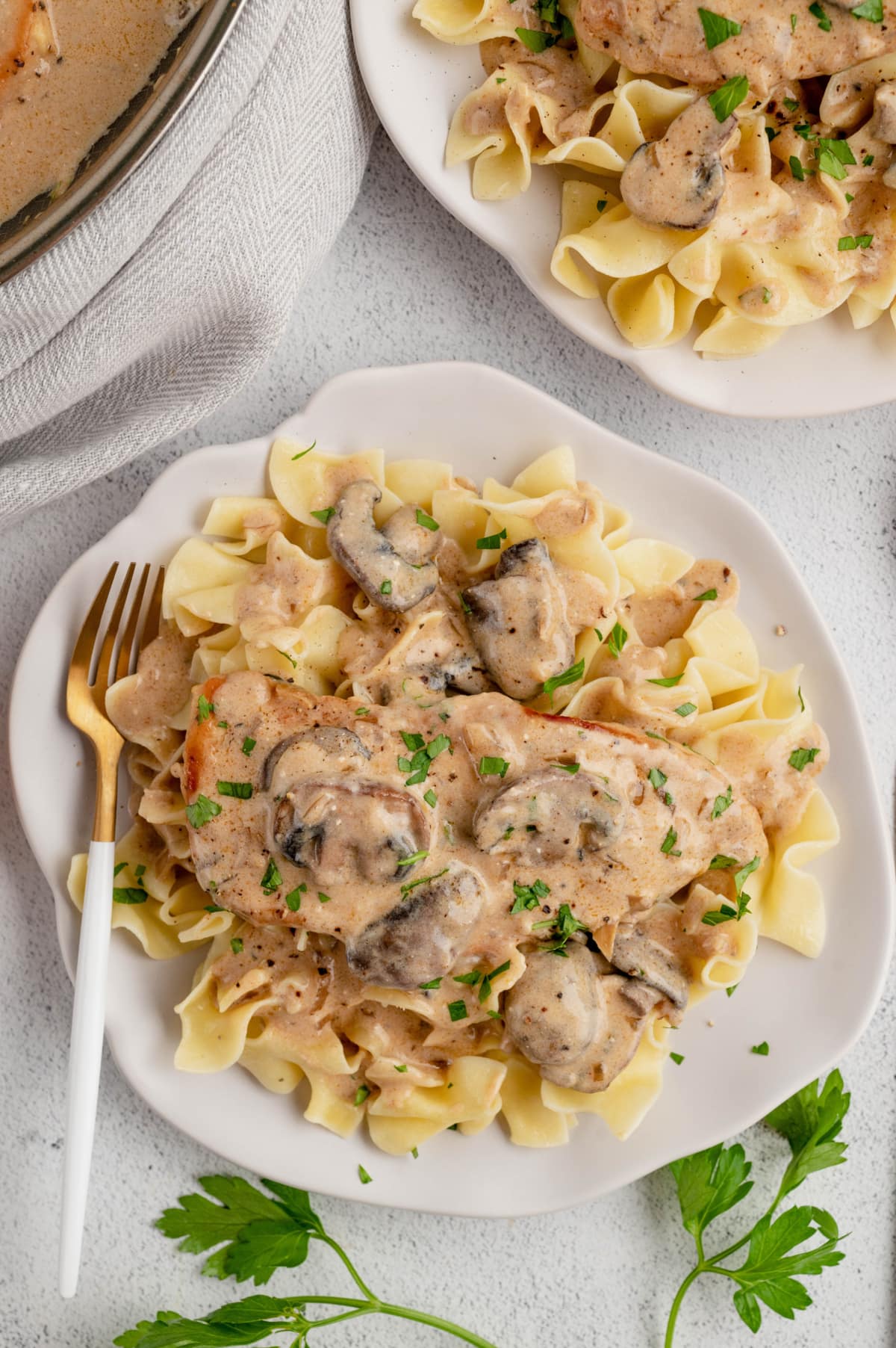 Chicken stroganoff over noodles on a white plate with a fork.