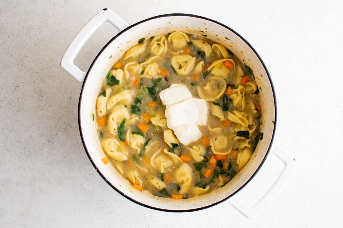 Cream cheese on top of a pot of tortellini soup.