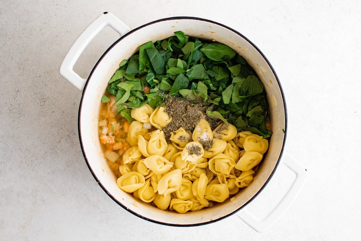 Veggies in broth, tortellini and spinach, in a soup pot.