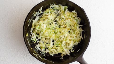 Shredded cabbage in a black skillet.