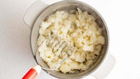 Mashing potatoes with a potato masher in a bowl.
