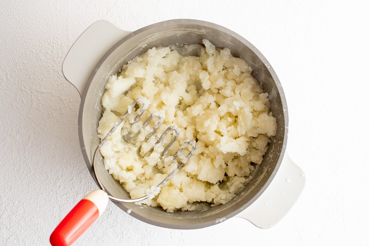 Mashing potatoes with a potato masher in a bowl.