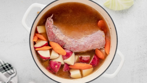 Corned beef in a pot of broth with carrots, potatoes and cabbage.