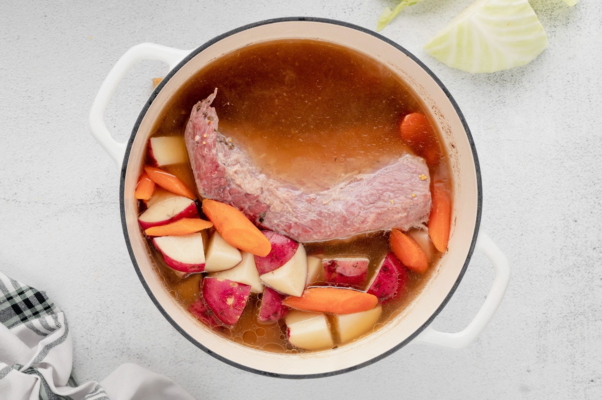 Corned beef in a pot of broth with carrots, potatoes and cabbage.