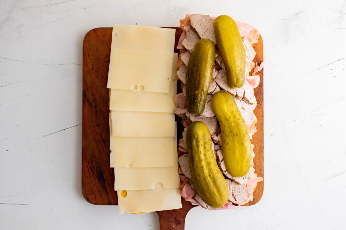Sliced cheese, pork and pickles on a loaf of bread.