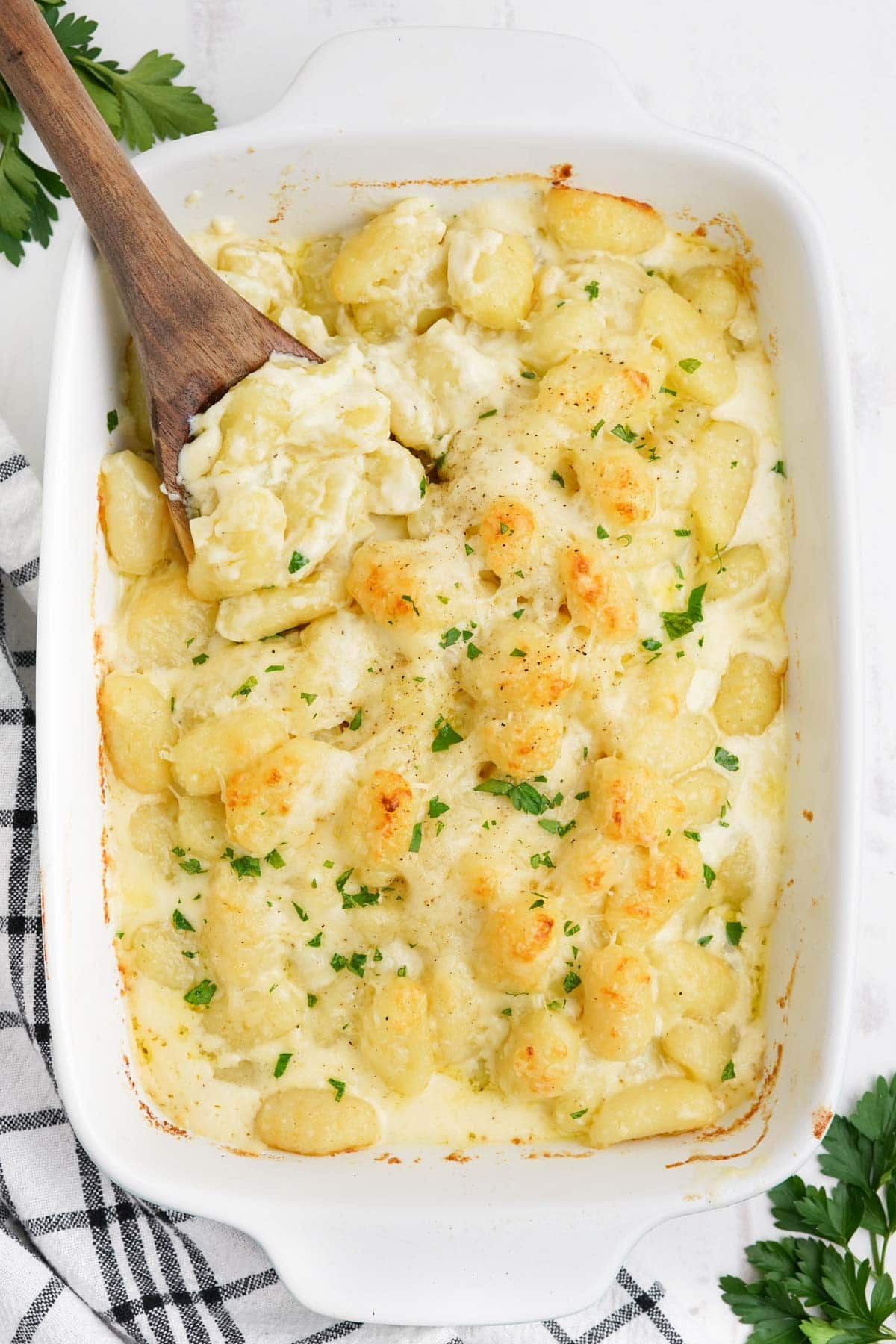 Baked casserole of gnocchi alfredo, golden on top, with a wooden spoon.