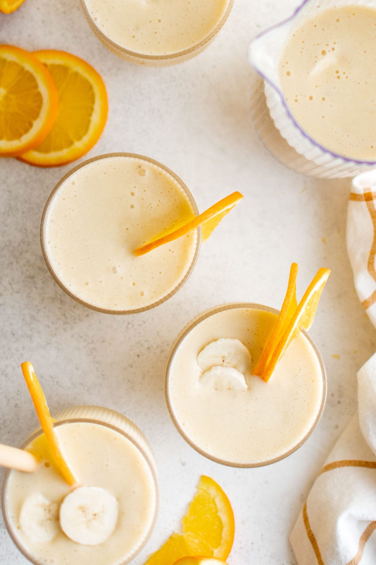 Overhead view of orange banana smoothie in glasses with slices of orange and bananas.