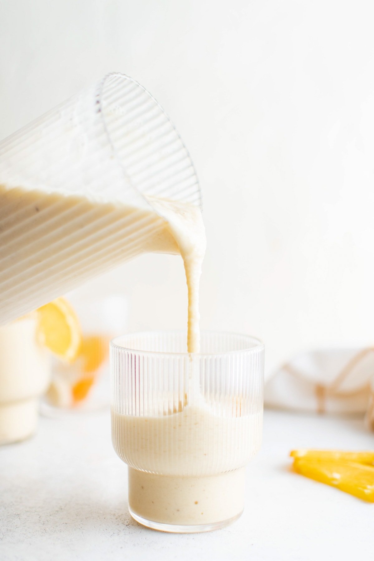 Blended smoothie being poured from a pitcher into a glass.