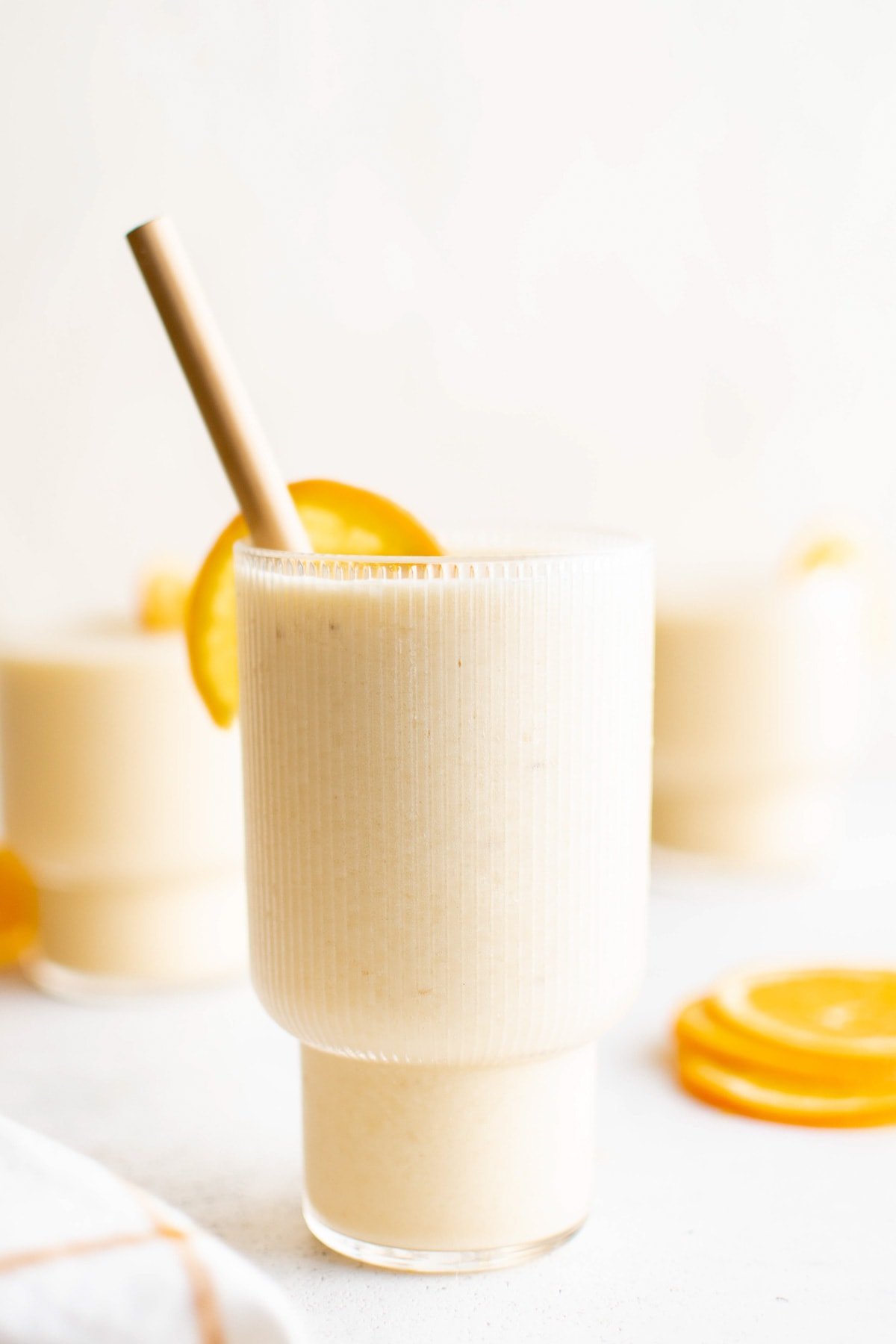 Smoothie in a glass with a slice of orange and a straw.