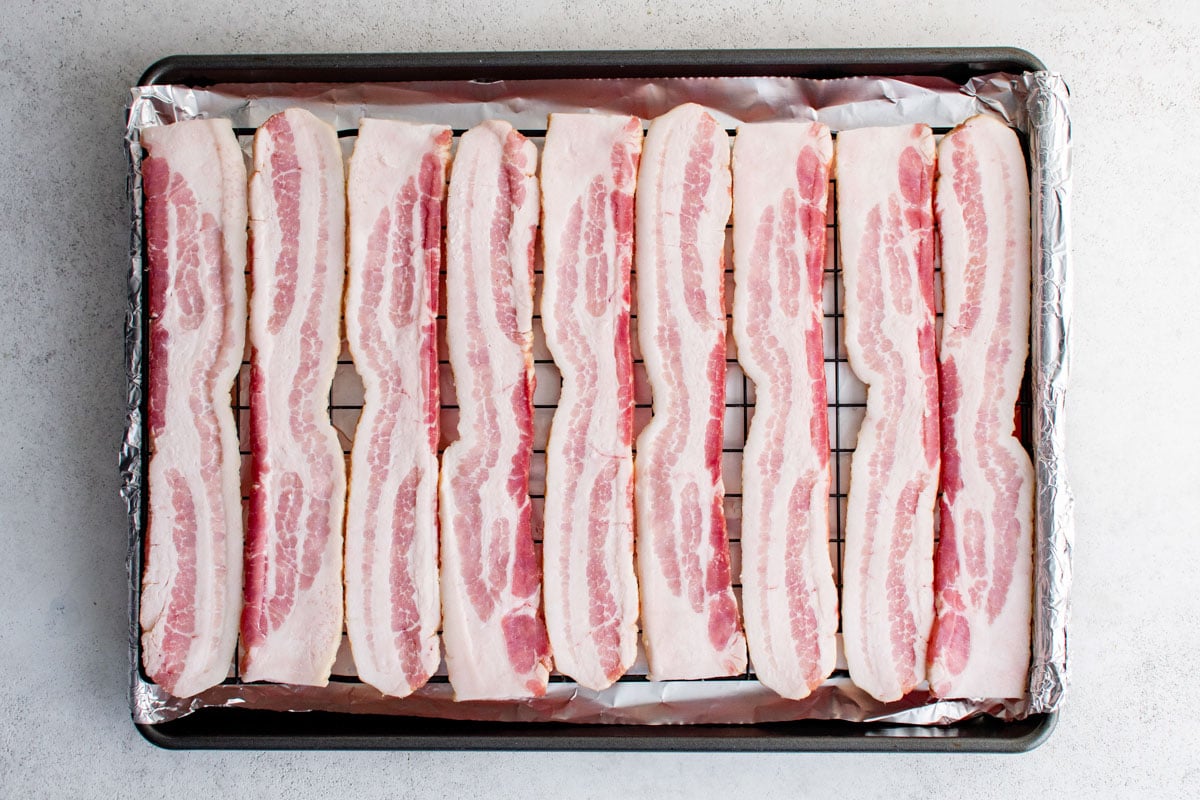 Raw bacon on a baking rack over a baking sheet.