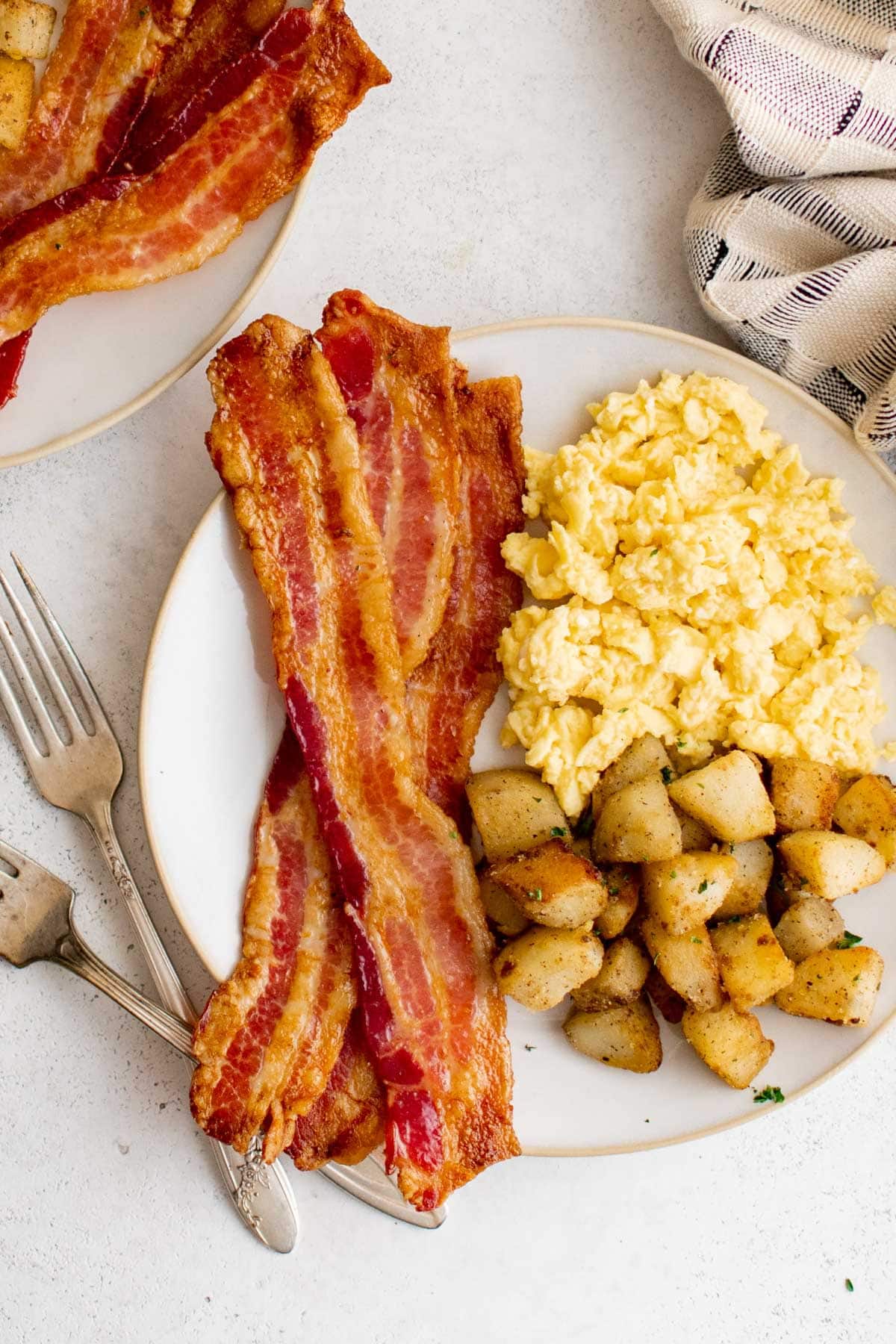 Bacon, scrambled eggs and diced potatoes on a plate with a fork.
