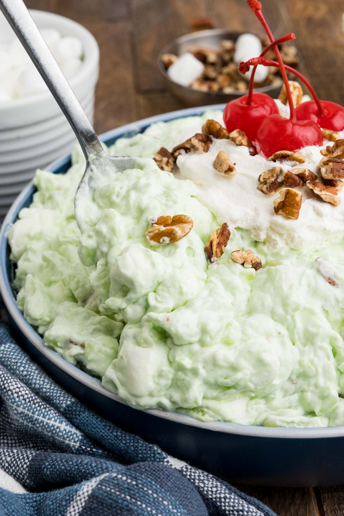 Pistachio salad in a bowl topped with pecans and cherries.