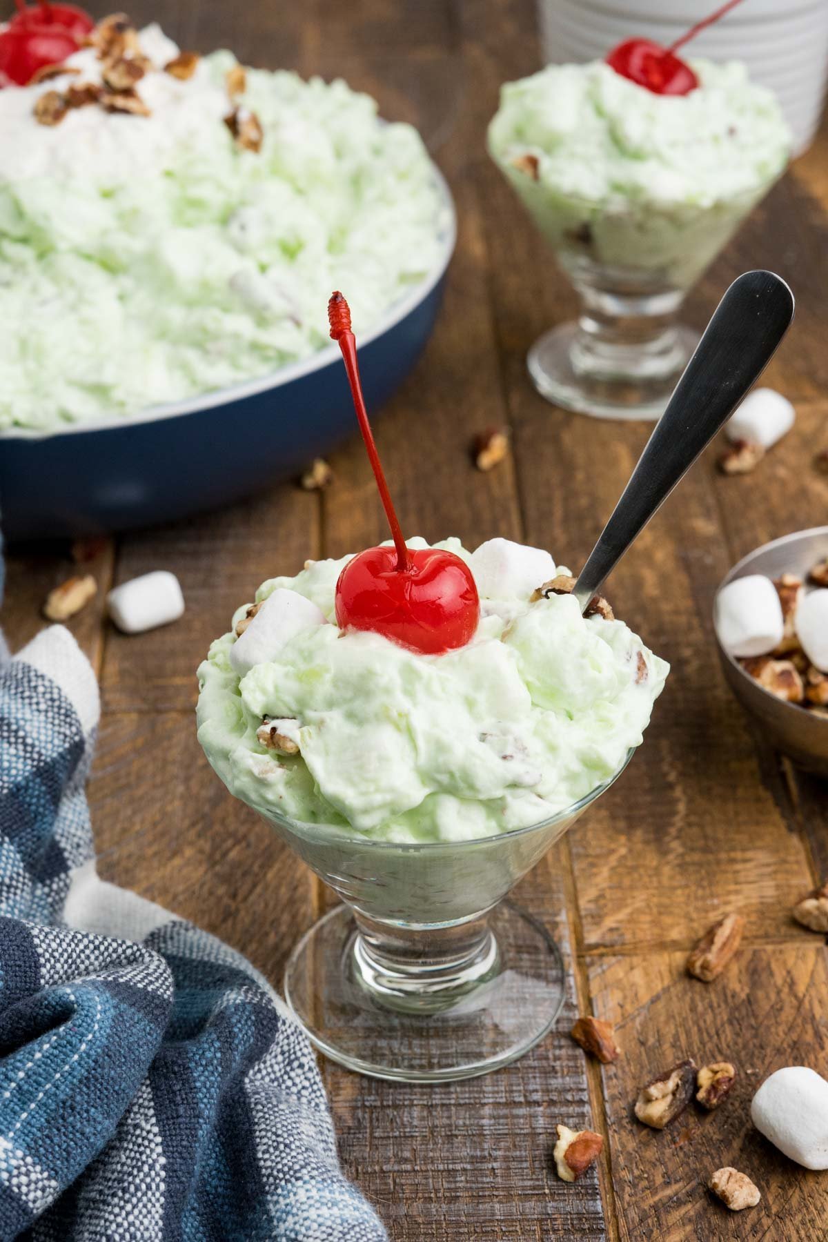 A small dish of pistachio salad with a cherry and a spoon.