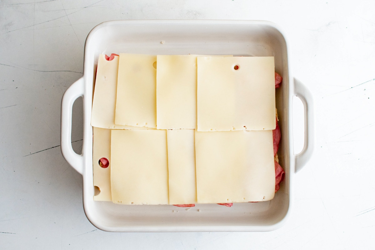 Corned beef and swiss cheese layered in a white baking dish.