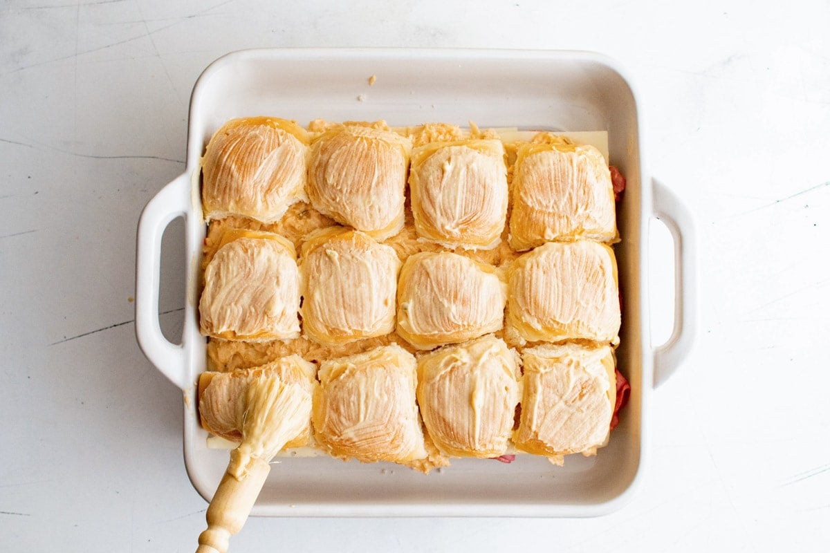 Rolls in a white baking dish., brushing on butter mixture.