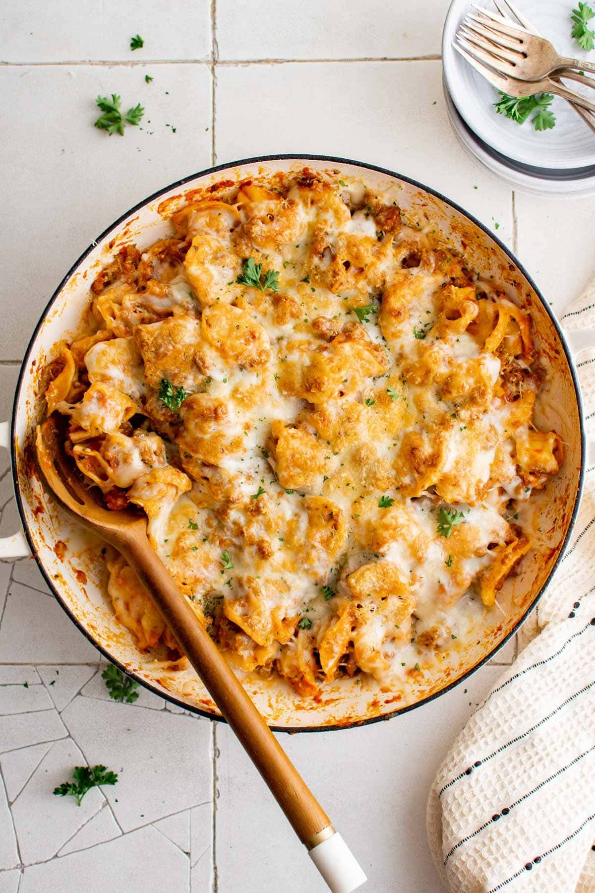 Tortellini and italina sausage in a large skillet with broiled cheese on top and a wooden spoon.