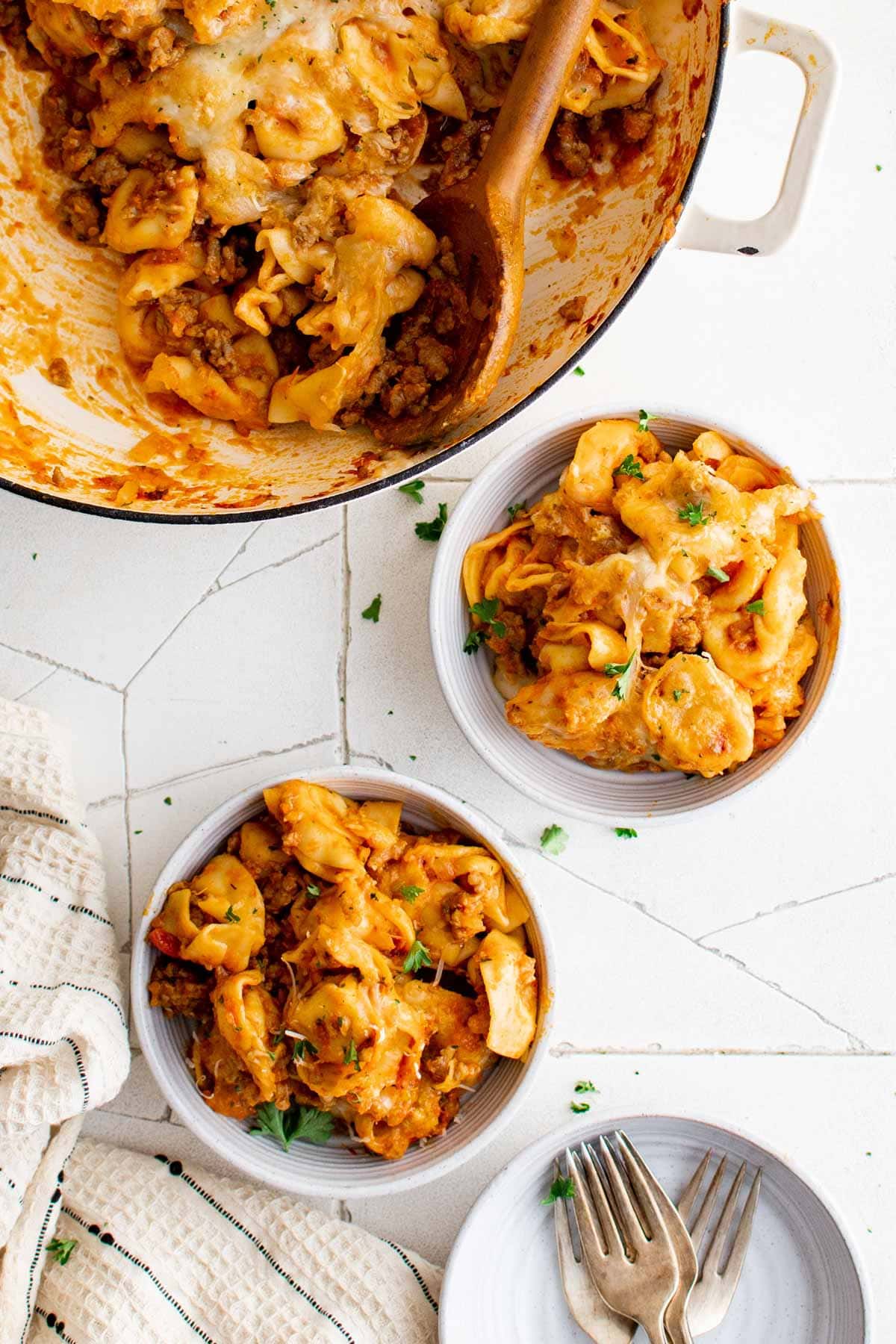 Tortellini and sausage served in bowls with forks.