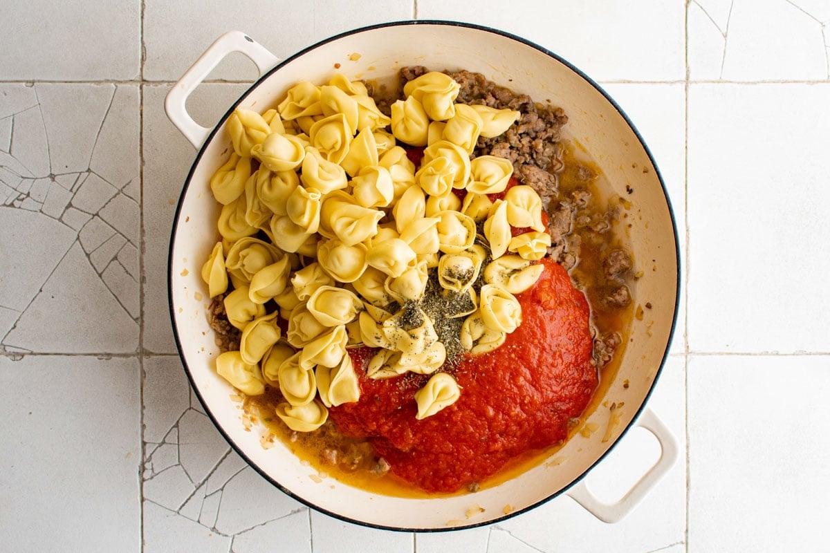 Tortellini, sauce and sausage in a skillet.