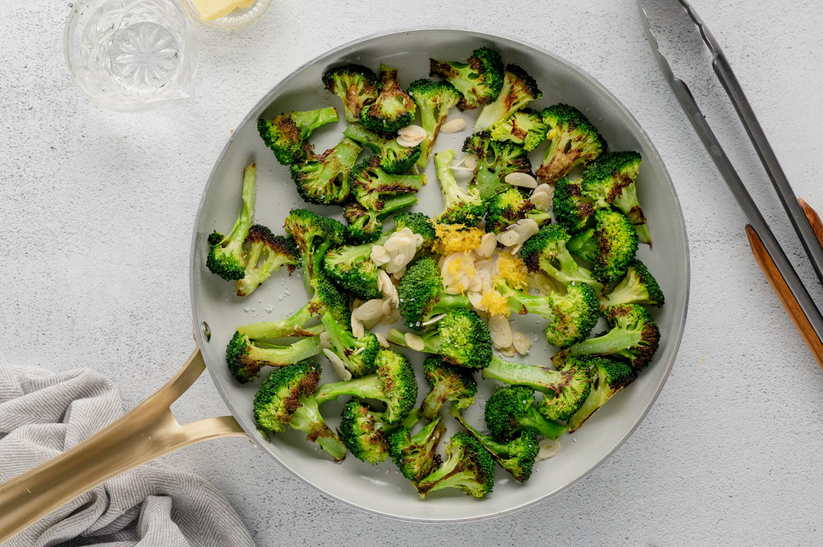 Broccoli in a skillet with sliced garlic and lemon zest.
