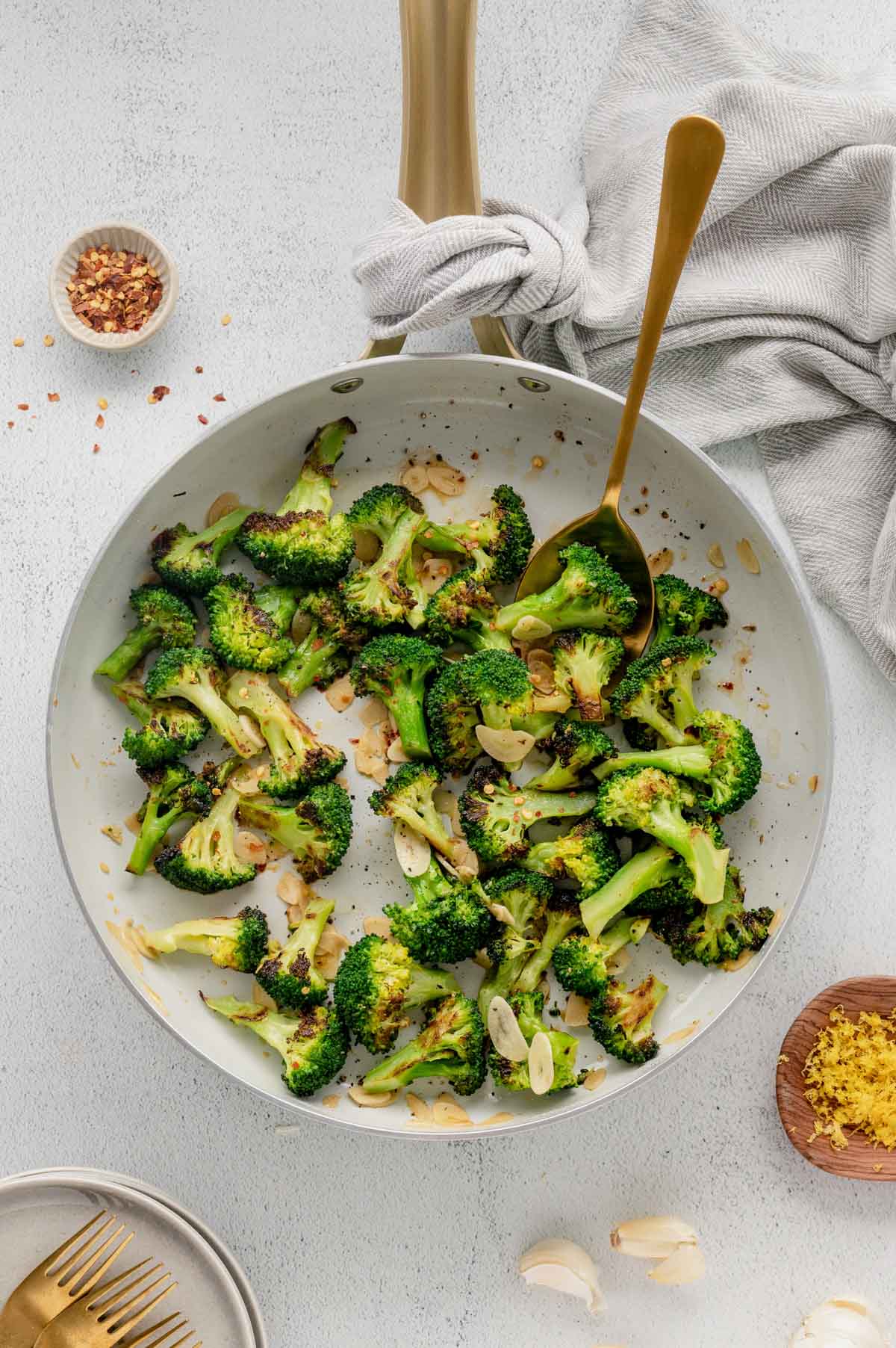 Sauteed broccoli with red pepper flakes in a white serving platter with a gold serving spoon.