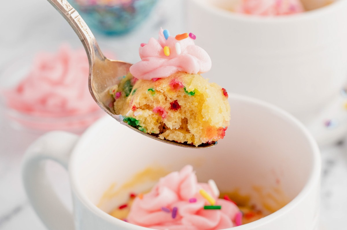 Mug cake with sprinkles, pink frosting and a spoon.