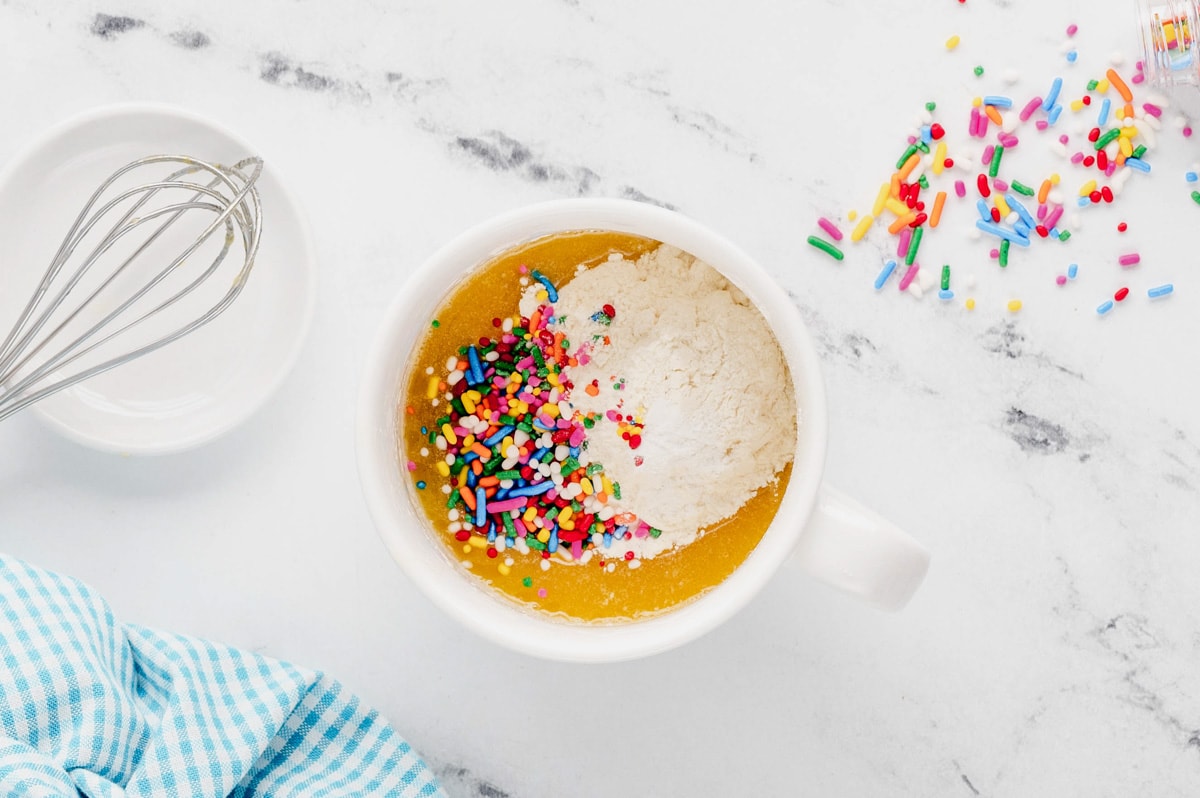 Melted butter and egg mixture, flour and sprinkles in a mug.