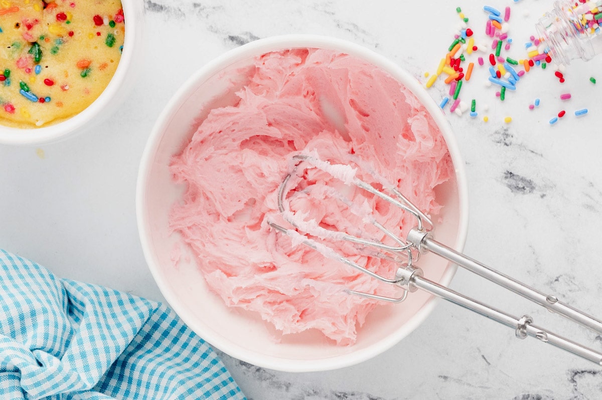 Pink frosting in a bowl with beaters.