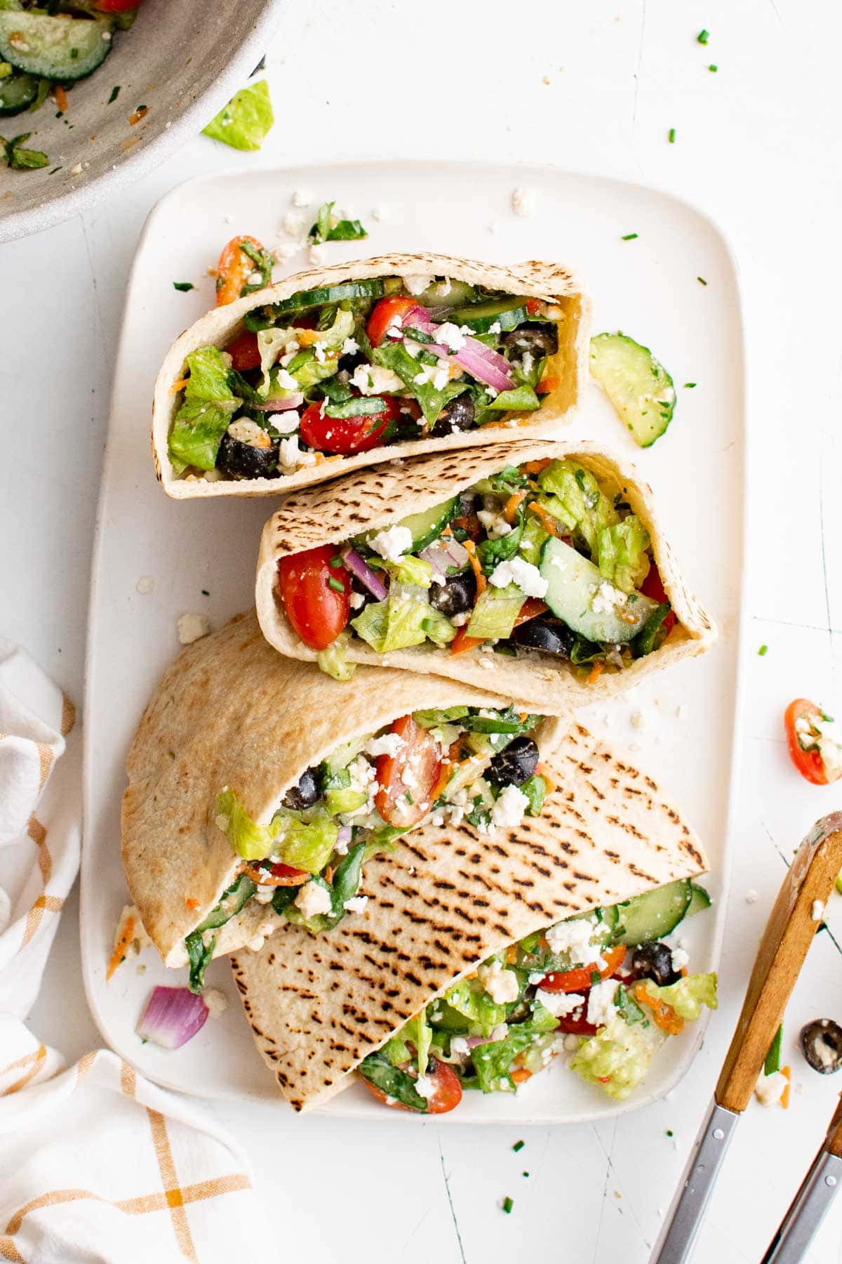 Pita pockets with fresh vegetables and feta cheese on a white platter.