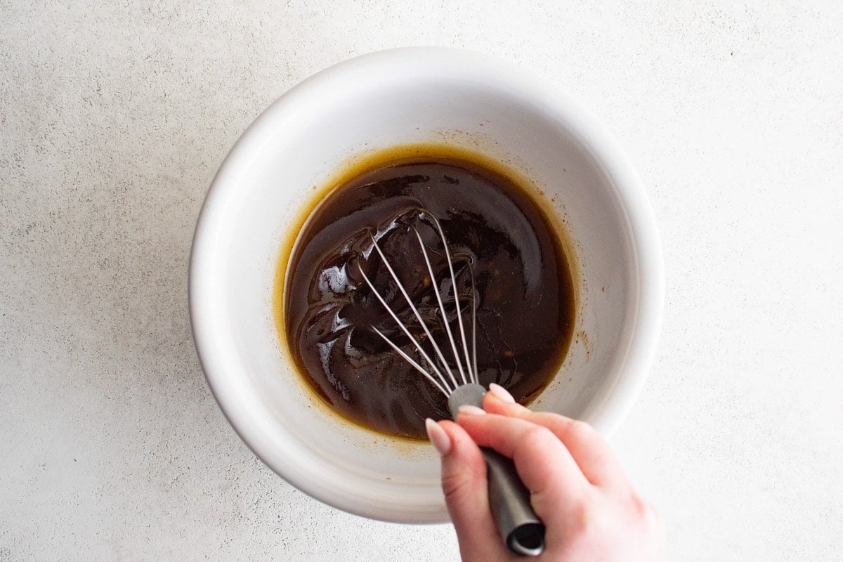 Whisking a balsamic vinegar and olive oil in a white bowl.