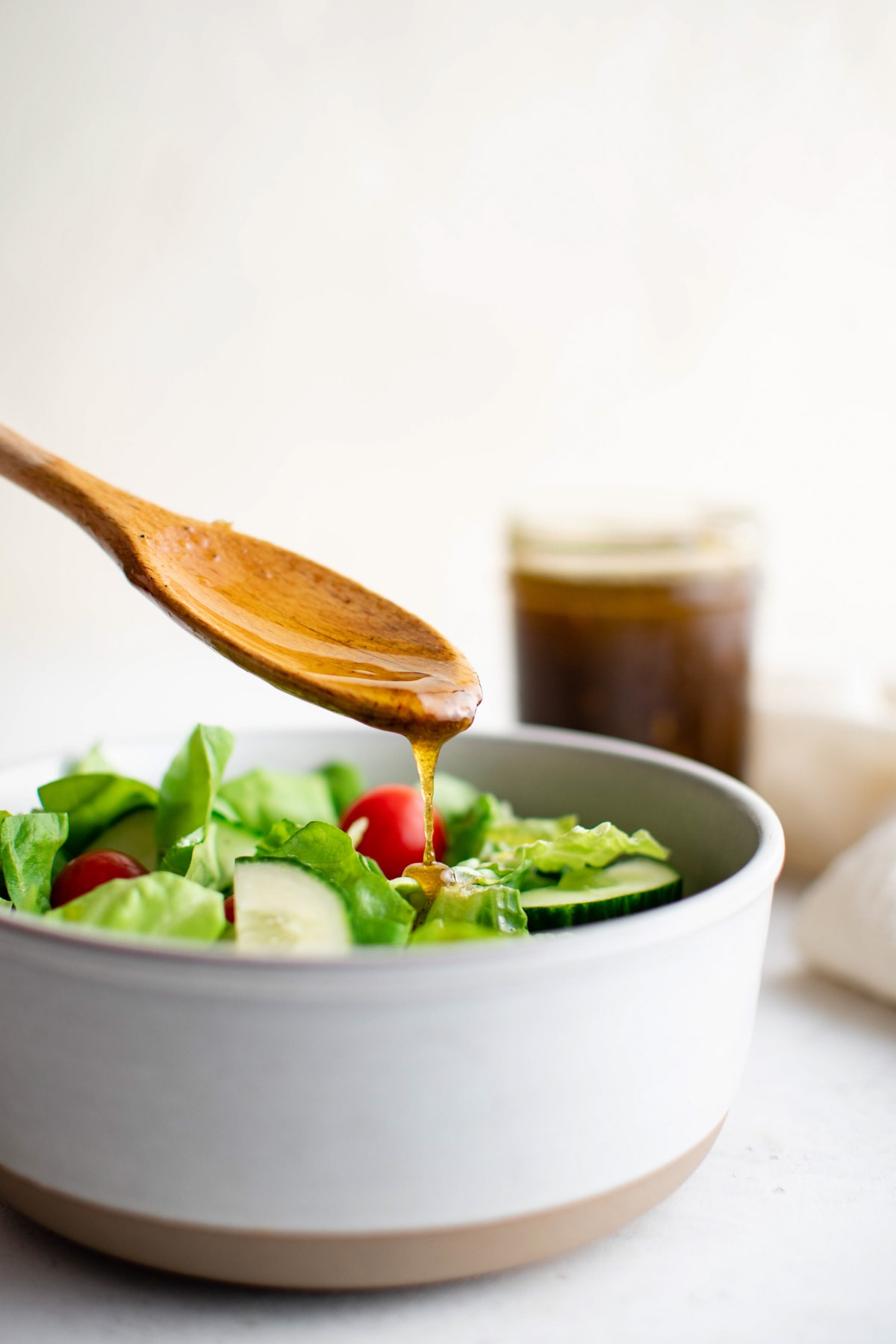 Wooden spoon drizzling balsamic vinaigrette voer a salad in a white bowl.