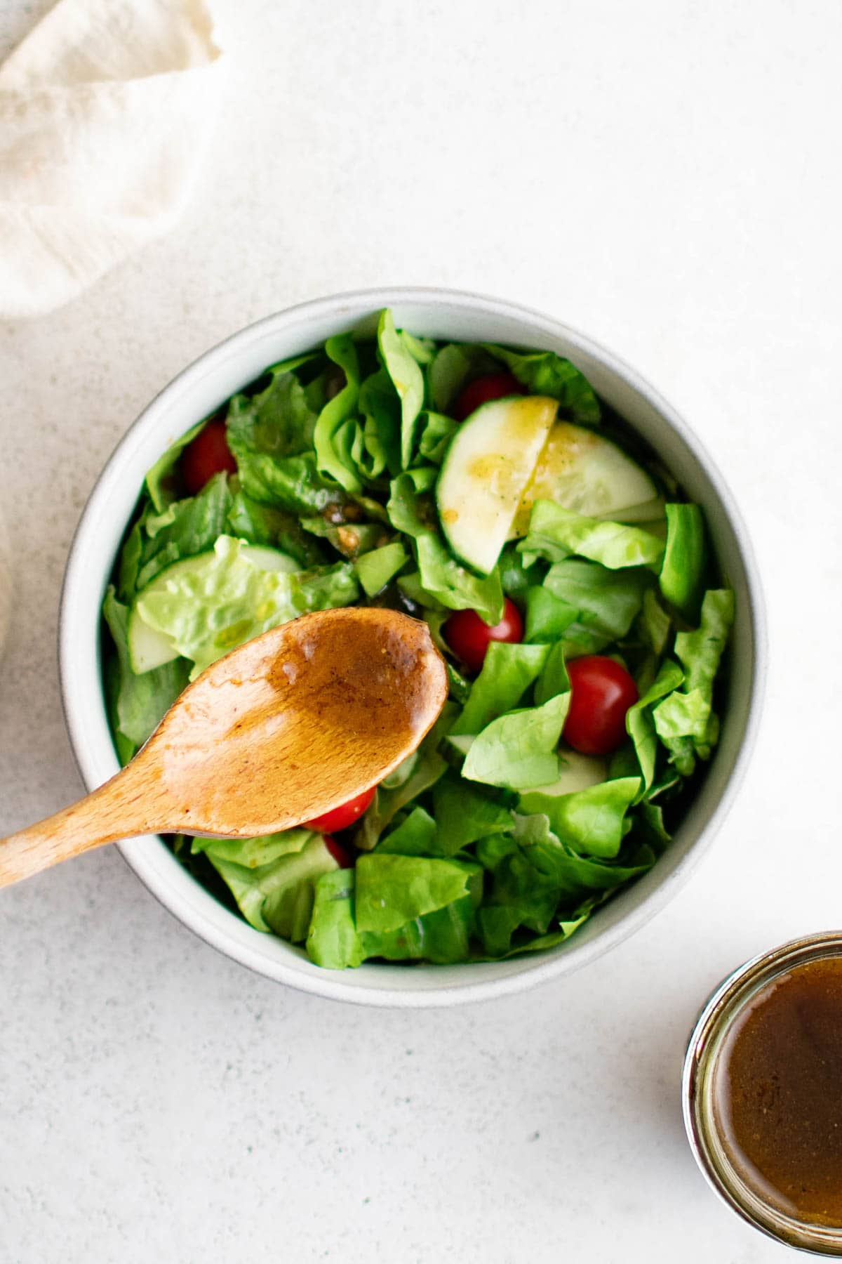 Salad in a white bowl with a wooden spoon and a little bit of vinaigrette dressing.