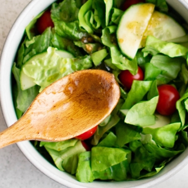Balsamic vinegar dressing on a wooden spoon over a salad.