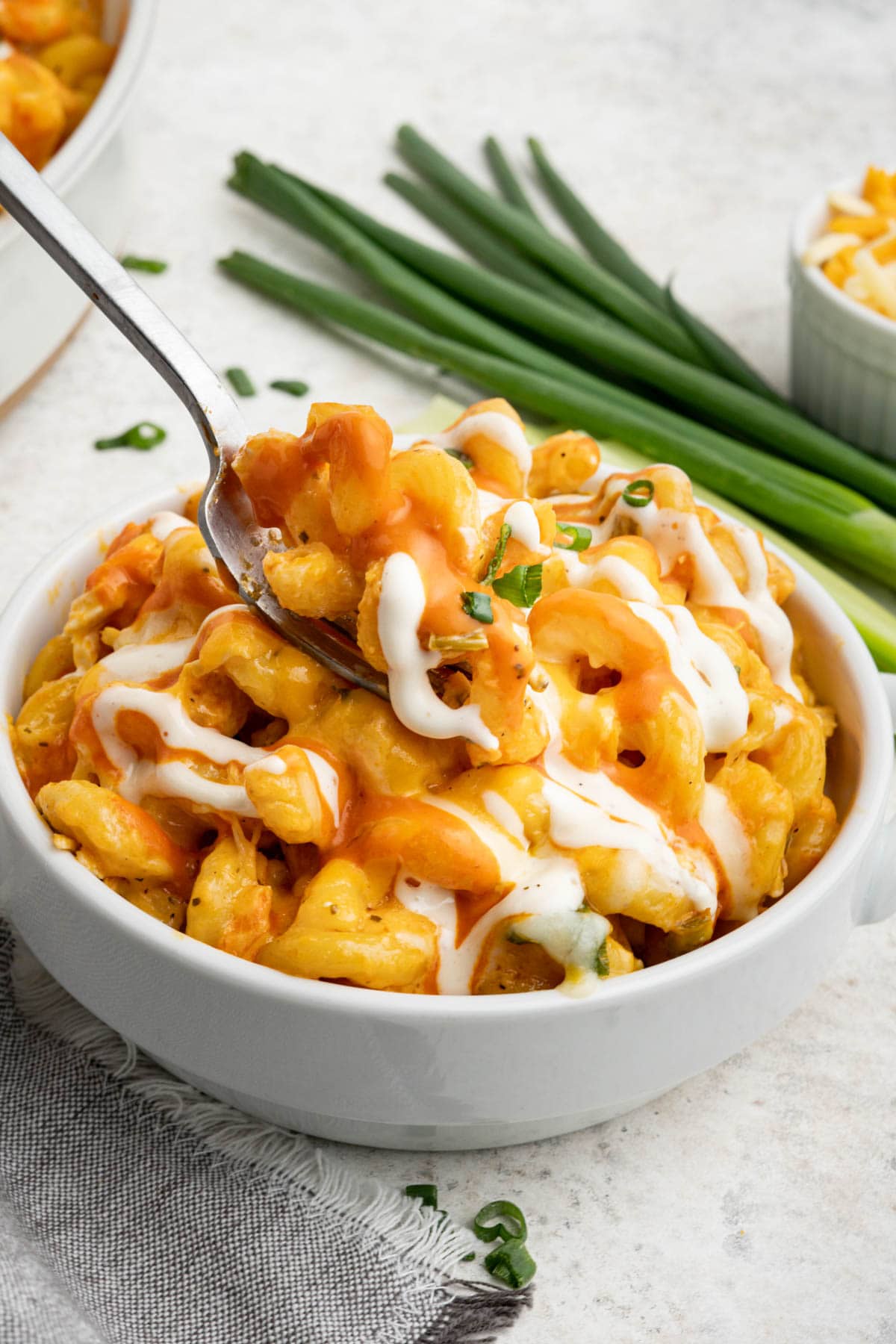Buffalo chicken pasta drizzled with ranch and served in a white bowl with a fork.