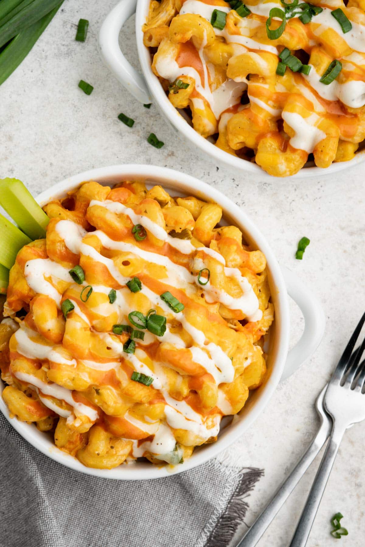 Buffalo pasta with cheese and chicken, drizzled with ranch and topped with green onions and celery in white bowls.