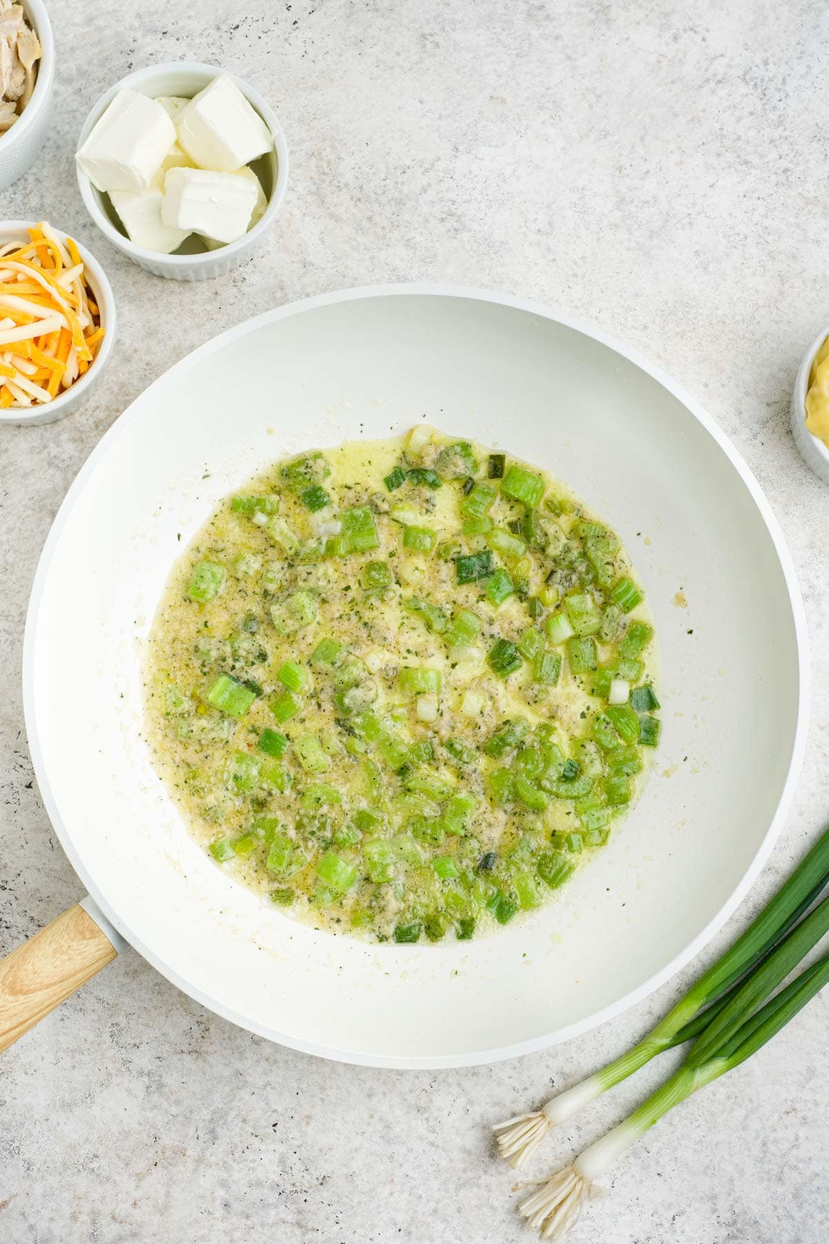 Green onions being sauteed in a white frying pan.