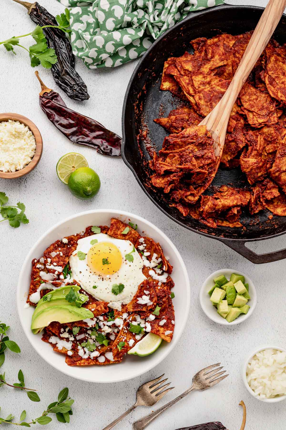 Chilaquiles rojas tortillas in a skillet with some in a bowl topped with avocado and eggs.