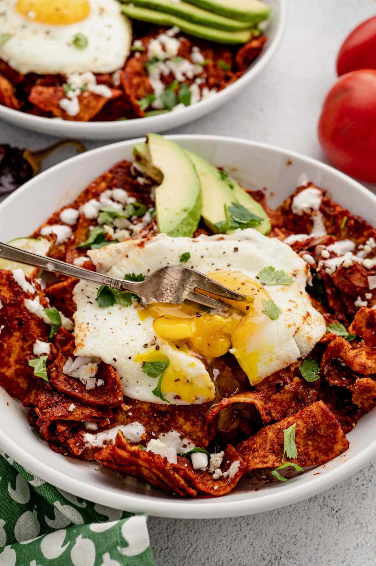Chilaquiles with a fried egg, cut into with a fork.
