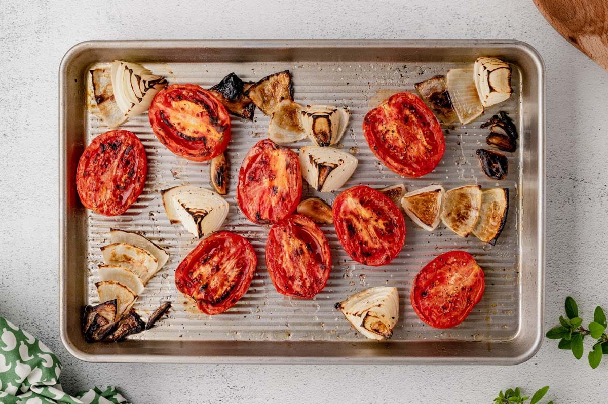 Roasted tomatoes, garlic and onion on a sheet pan.