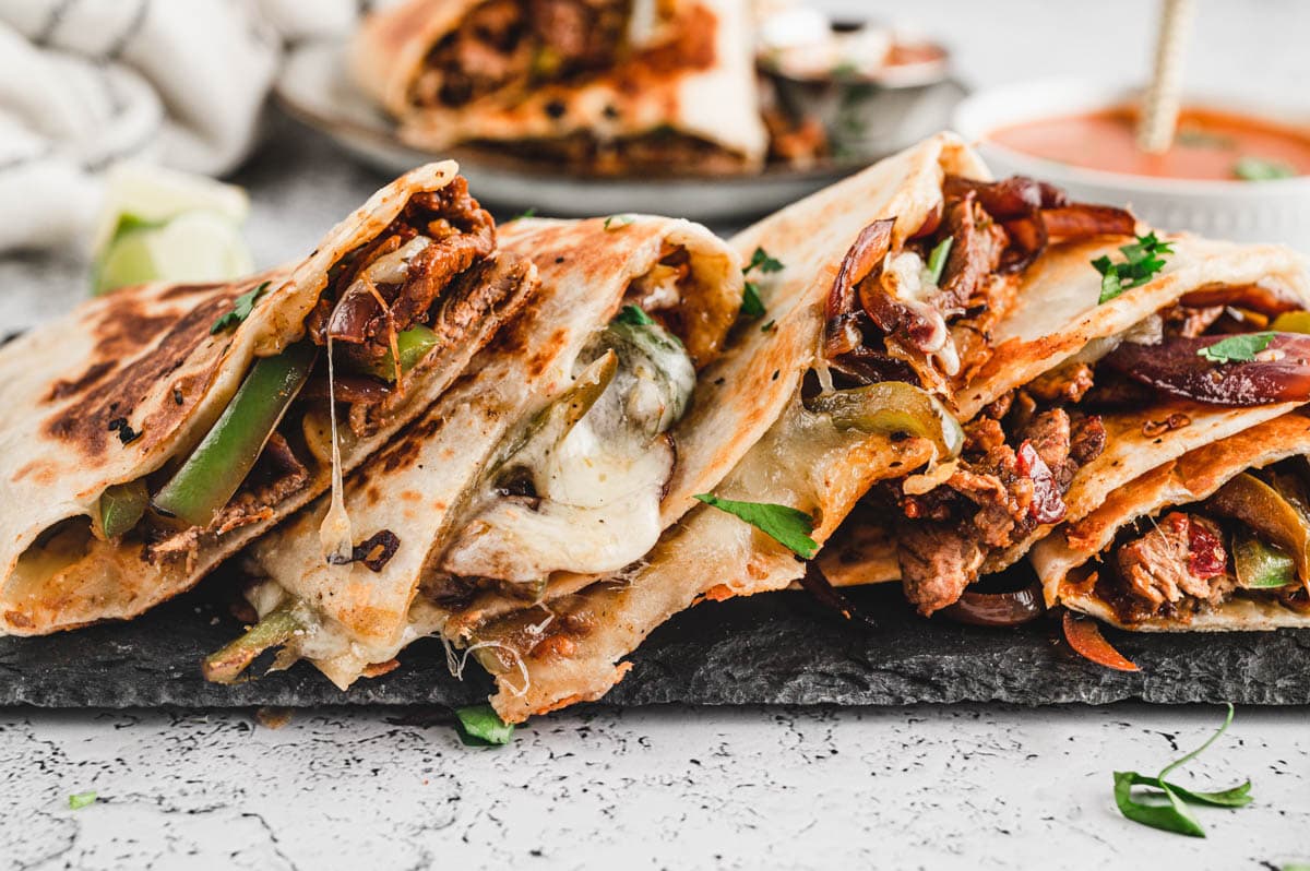 cut up quesadillas stacked side by side on a platter with gooey cheese.