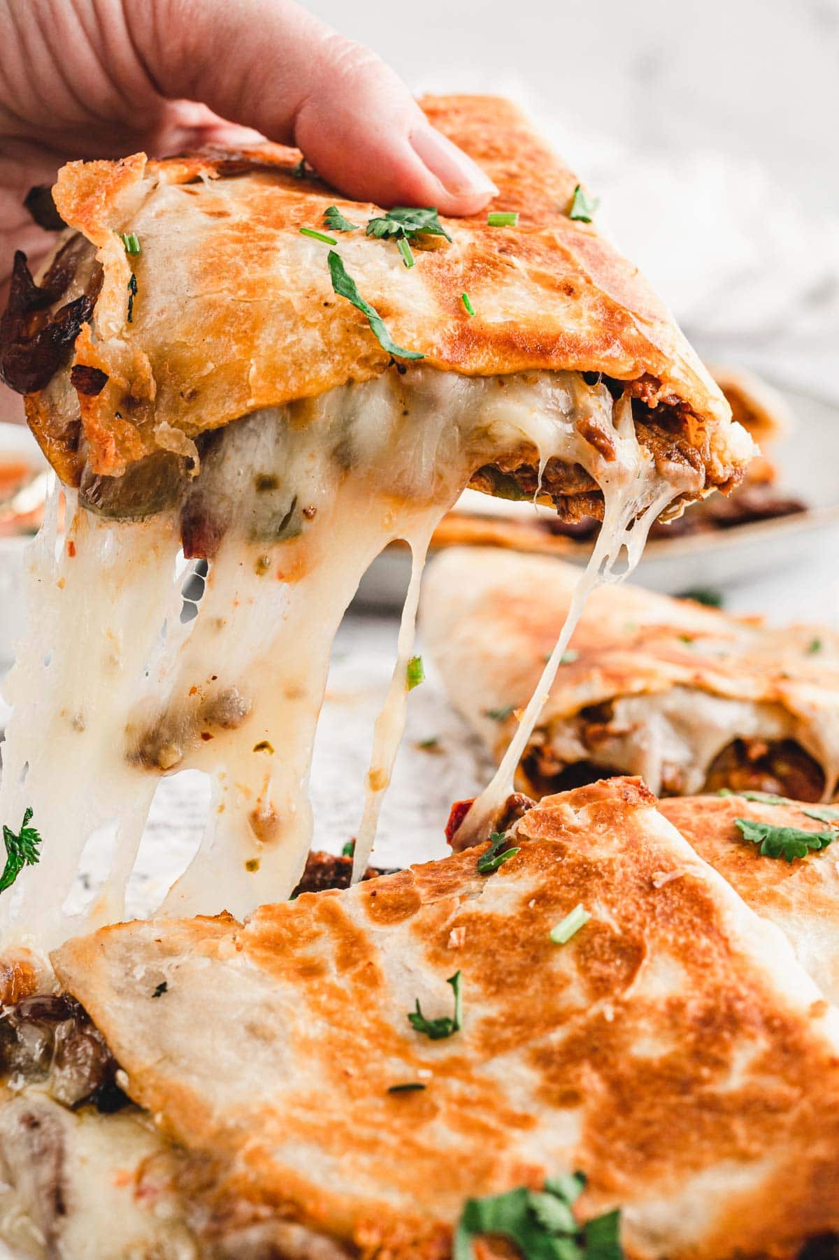 A slice of quesadilla being pulled upward to reveal the gooey cheese.