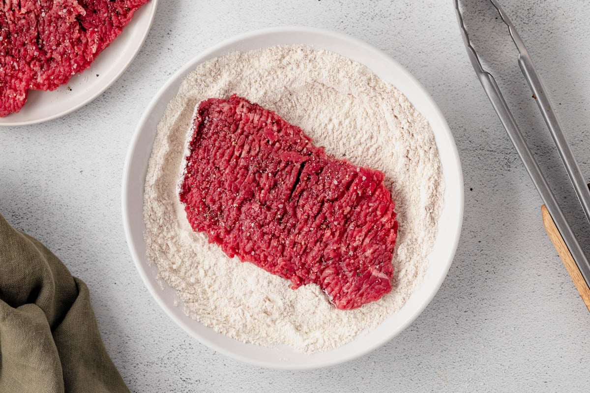 Cube steak sitting in a dish of flour.