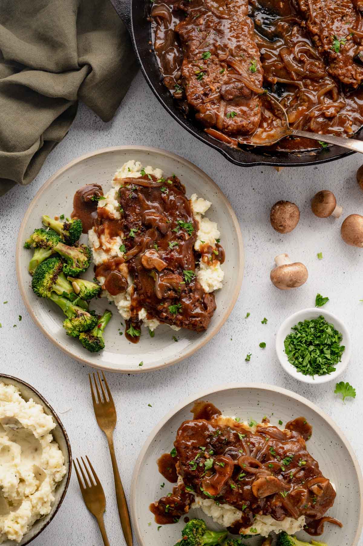 Cube steaks and gravy with mashed potatoes and broccoli on white plates.