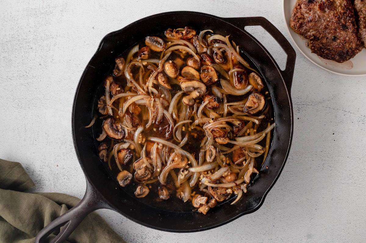Mushrooms and sliced onions being sauteed in a cast iron skillet.