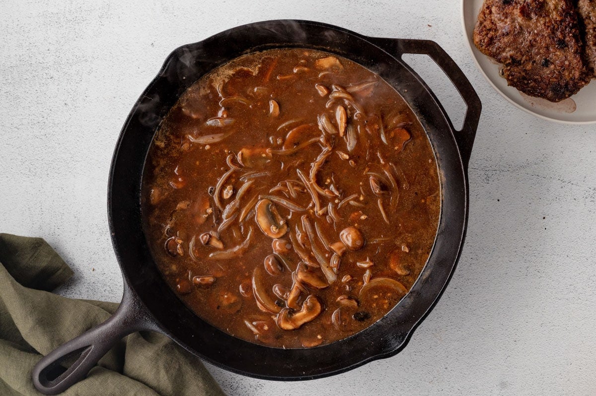 Brown gravy with onions and mushrooms in a skillet.