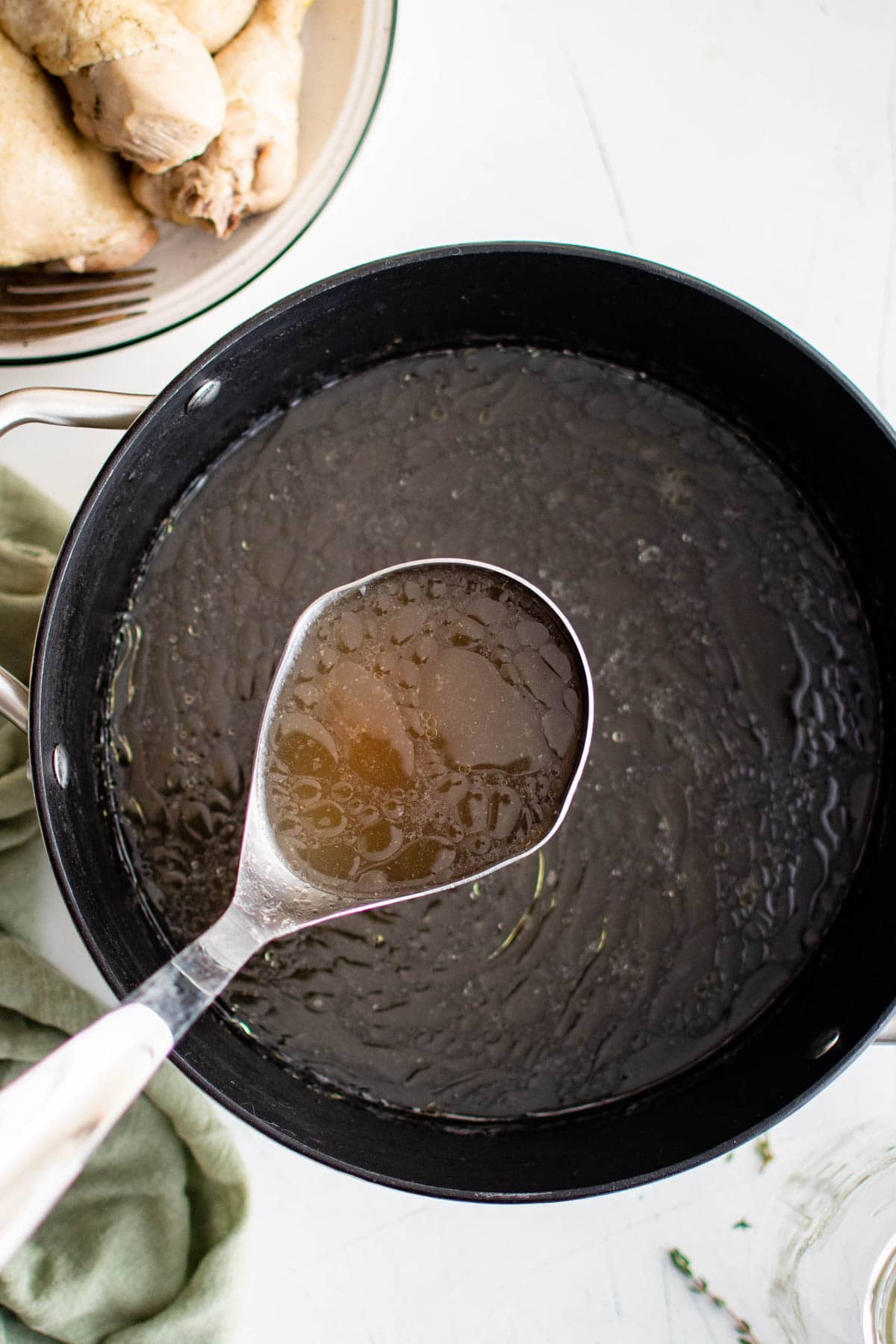 Clear chicken broth in a ladle over a pot.