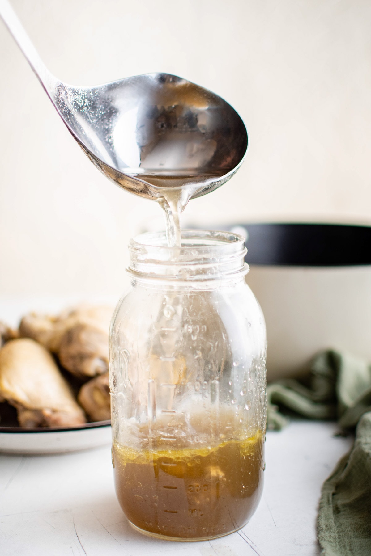 Ladle pouring chicken broth into a large mason jar.