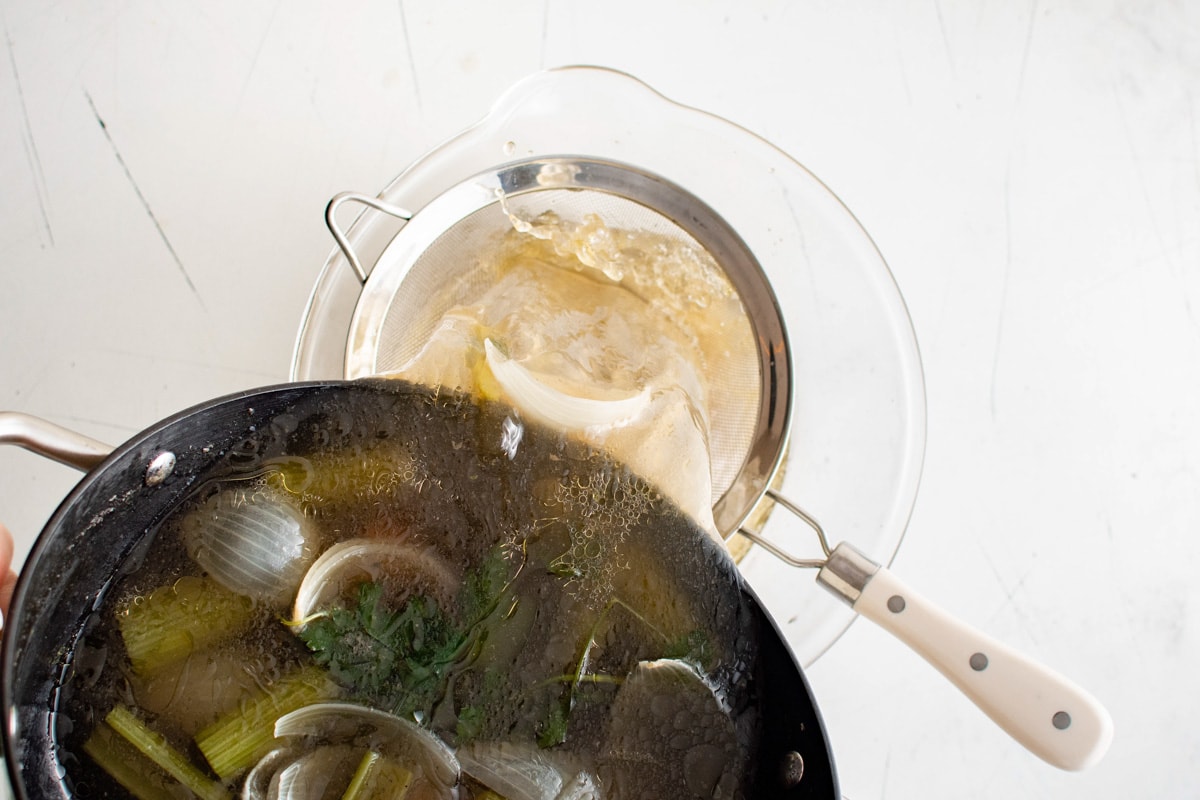 Straining homemade chicken broth from a soup pot into a mesh sieve.