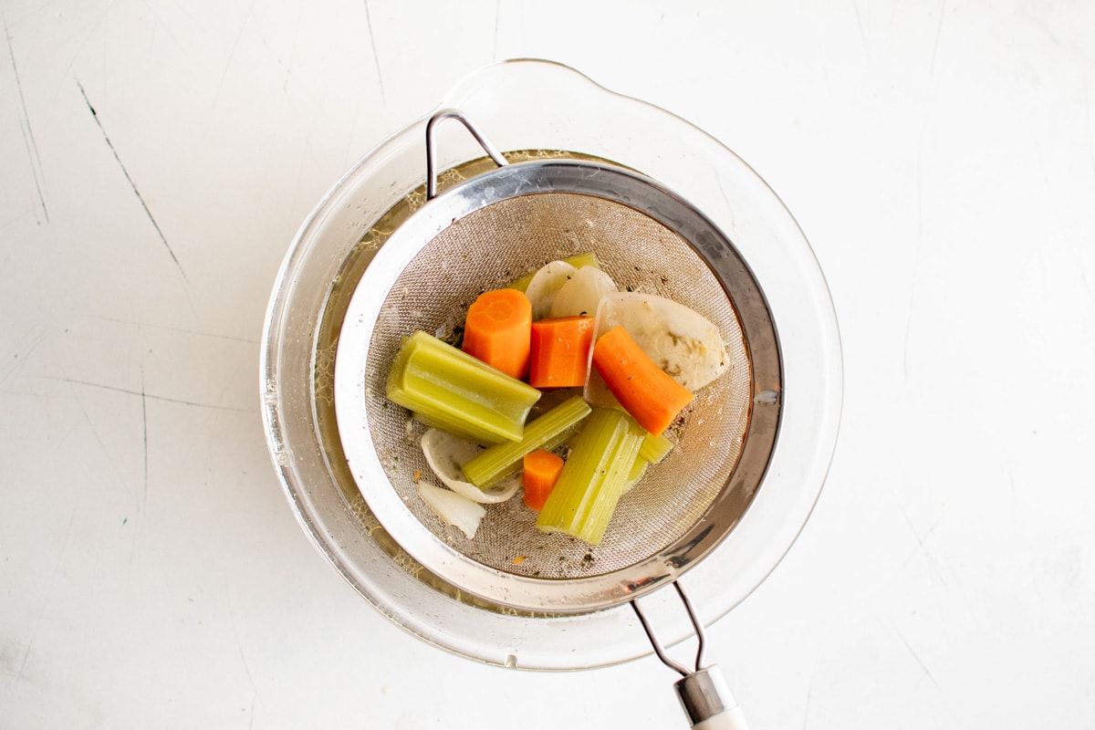 Carrots, celery and onions in a mesh sieve over a bowl.