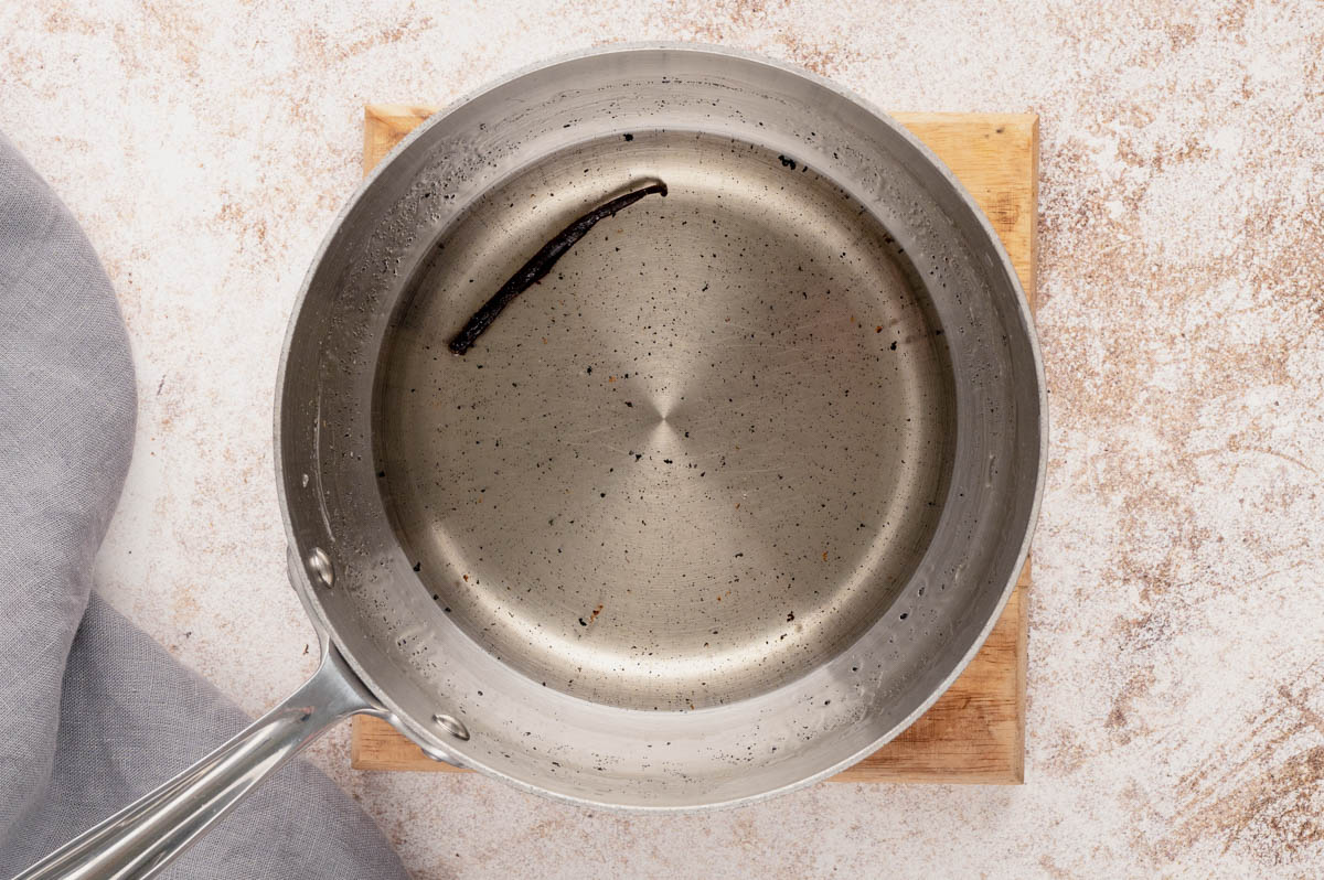 Vanilla bean pod floating in a clear liquid in a saucepan.